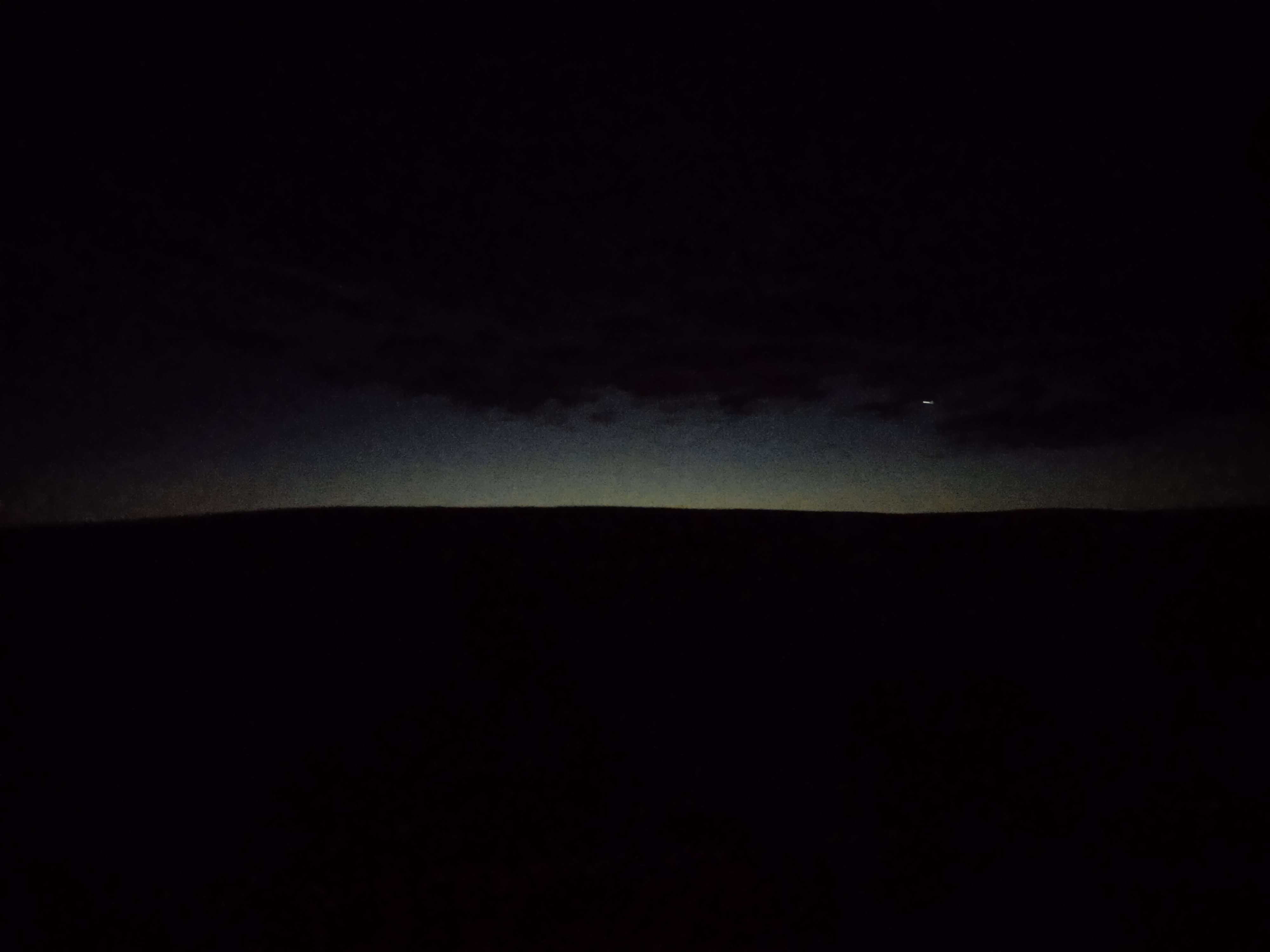 a cloudy and dark landscape, the only light coming distantly from over a hill.